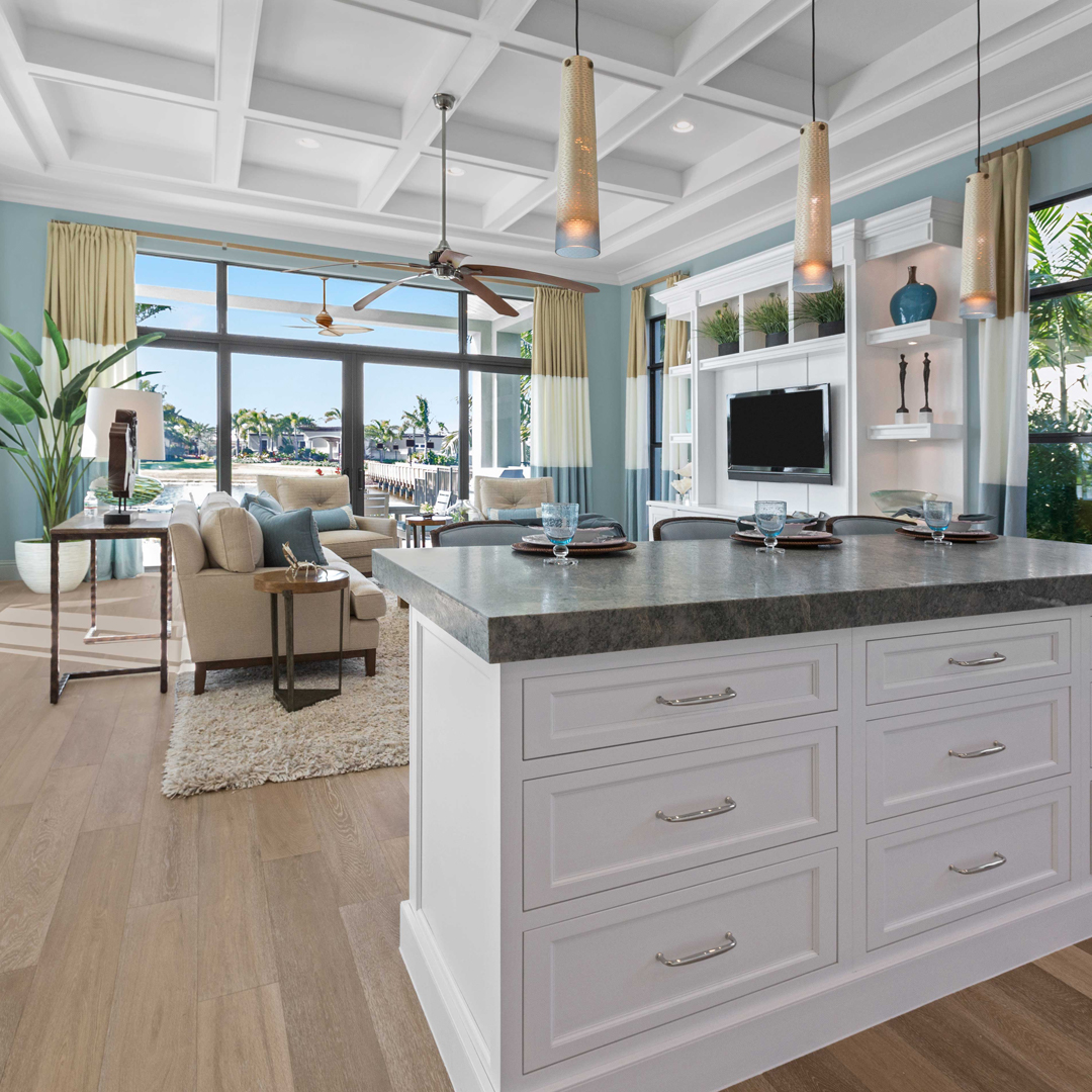 bright white kitchen with a large island in the middle, with natural light coming in the windows from the living room